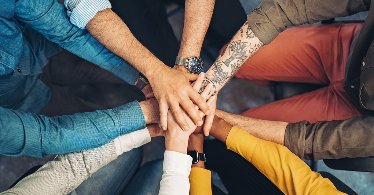 A diverse group of people putting their hands on top of one another in a circle.