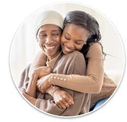 An older Black woman wearing a headscarf being hugged by her daughter.