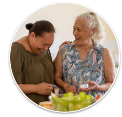 An elderly Asian woman laughing with her adult daughter in a home kitchen environment.