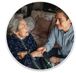 An elderly Asian woman sitting with a blanket over her lap, smiling and talking to a young adult male.