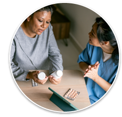 A middle-aged woman of color holds two pill bottles as she talks with a health care professional wearing blue scrubs.