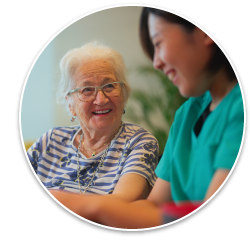 A senior woman smiling at a nurse/home aide in scrubs as they make origami together.